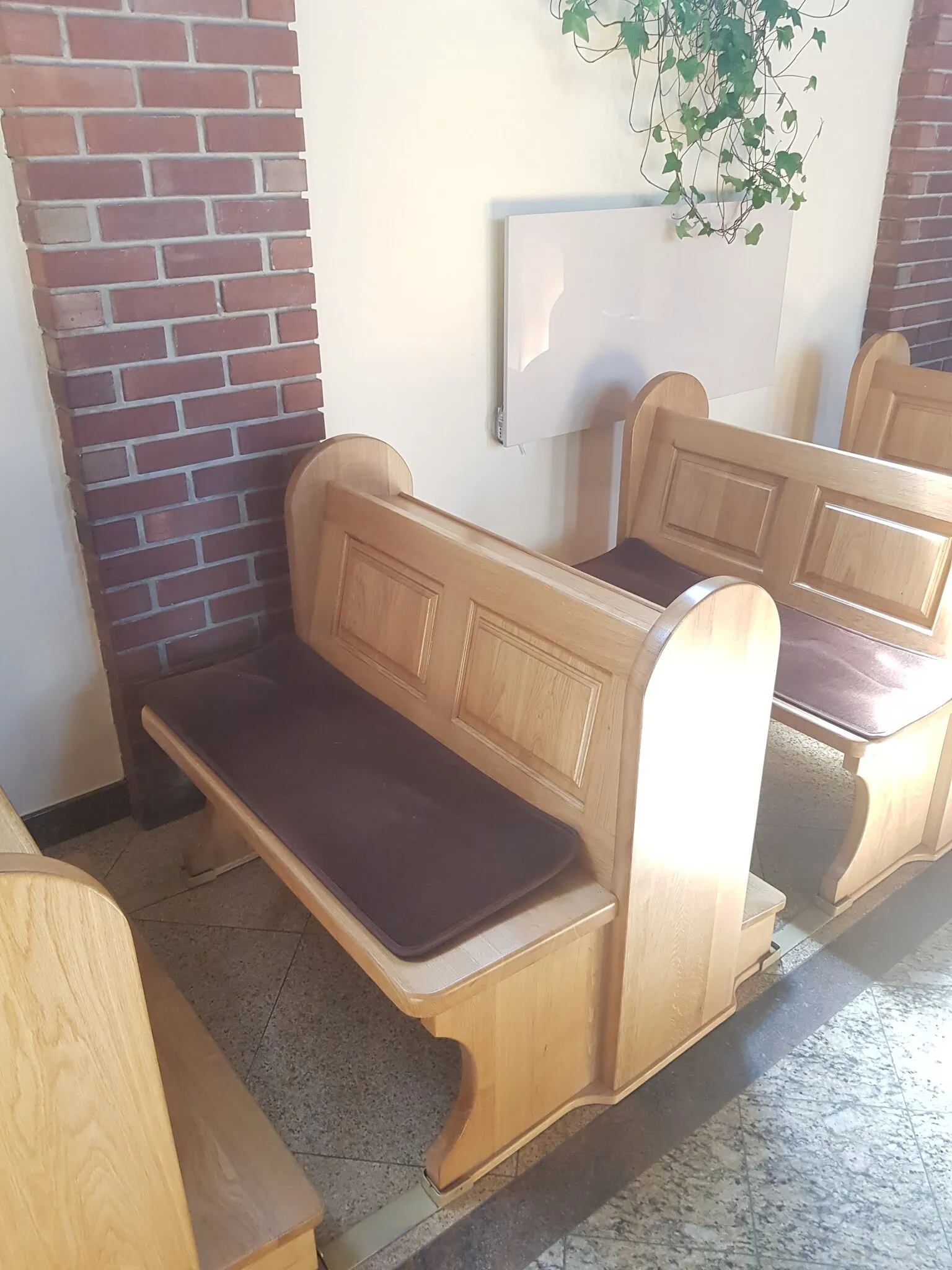 Ławka ustawiona przy ceglanym filarze, widoczna listwa mocująca w posadzce